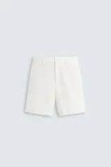 Bermuda de algodón color blanco, de corte relajado, con cintura elástica, bolsillos frontales y bolsillos traseros de plastrón. Cierre frontal con cremallera y botón.