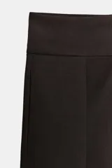 Pantalón negro de tiro alto, corte amplio estilo balloon o culotte, con pliegues marcados en el delantero y bolsillos laterales ocultos.