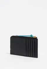 Billetera de cuero vacuno en color negro con bolsillo exterior en color naranja y tirador de cierre en color turquesa. Cuenta con logo de la marca estampado en dorado.