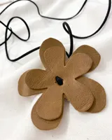 Gargantilla con dije de flor de cuero color marrón y tira de cuero negra. El largo de la tira es de 140cm y el dije mide 9x9cm.