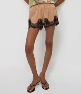 Short de satén color beige con acabado brillante, corte holgado, cintura elástica y detalle de encaje floral negro en el bajo.