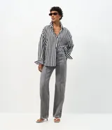 Pantalón wide leg de tiro alto confeccionado en denim de algodón. Presenta un diseño con friso vertical en el frente, cierre de botón y cremallera, trabillas en la cintura y bolsillos funcionales en la parte delantera y trasera.