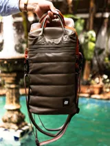 Bolso matero negro de cuero sintético con diseño capitoneado, correa larga regulable y doble asa corta.