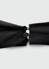 Top de satén negro con escote halter y cuello drapeado. Presenta un diseño sin mangas, espalda abierta y bajo asimétrico con cierre de botones en la parte posterior.