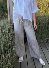 Pantalón de corte ancho y relajado, confeccionado en lino con diseño de rayas verticales. Presenta cintura elástica con cordón de ajuste y bolsillos laterales.