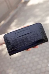 Billetera mediana de cuero negro con textura tipo cocodrilo y cierre perimetral con cremallera. Tiene el logo de la marca grabado en la parte frontal.