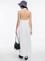 Vestido largo de lino en color azul, con cuello camisero, cierre frontal de botones y espalda descubierta con diseño estilo halter. Presenta un bordado decorativo en el cuello y bolsillos laterales.