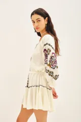 Vestido corto de bambula color celeste, con escote redondo, mangas tres cuartos abullonadas y falda con volado en el ruedo. Presenta bordados decorativos en el frente y las mangas, y cuenta con un cinturón de la misma tela para ajustar a la cintura.