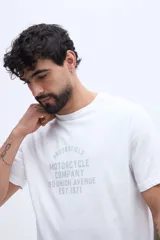 Remera blanca de manga corta con cuello redondo y estampa frontal de estilo vintage con texto inscripto.