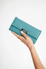 Monedero tipo sobre color celeste, con cierre de broche imantado y logo de la marca en placa metálica plateada. Interior con tarjetero, espacio para billetes y bolsillo con cierre.