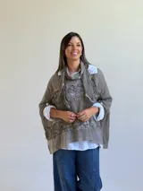 Sweater de punto color visón con diseño superpuesto, que incluye una bufanda integrada y detalles de encaje floral en el frente. Presenta mangas tres cuartos con puños abotonados y un corte holgado.