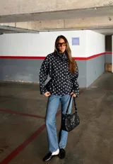 Campera de algodón con estampado de lunares blancos sobre fondo negro. Presenta cuello alto, cierre frontal con botones metálicos y cinturón ajustable en la cintura. Posee bolsillos laterales y un diseño versátil que permite llevarla entallada o con silueta holgada.