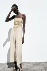 Pantalón de lino negro, de tiro alto, con bolsillos delanteros de vivo, pernera recta y cierre frontal con cremallera, botón interior y gancho metálico.