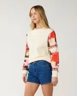 Buzo de cuello redondo color off white, con mangas largas estampadas con diseño patchwork multicolor en tonos rojos, rosas y negros.