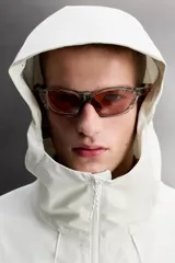 Cazadora deportiva de ajuste regular, confeccionada en tejido técnico de tres capas con membrana impermeable (resistencia al agua ≥15K) y costuras termoselladas. Presenta cuello subido con capucha ajustable, manga larga con puños ajustables con tira adherente, aberturas con cremallera termosellada en axilas para ventilación, bolsillos frontales con cremallera termofijada y bajo ajustable con elásticos laterales.