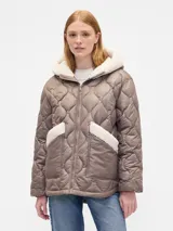 Campera acolchada color beige con diseño de costuras onduladas, cierre frontal, capucha y bolsillos frontales con detalles en corderito blanco.