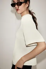 Camisa de cuello subido y manga corta con hombreras. Presenta un diseño minimalista con cierre de cremallera metálica en la espalda.