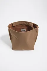 Bolso bandolera de tamaño mediano de la marca Bimba y Lola, color marrón, con exterior de nylon, correa ajustable de lona en tono tostado y detalles de metal dorado. Incluye cierre superior y el logo de la marca estampado en el frente.