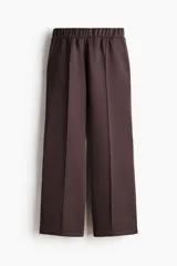 Pantalón de corte holgado en punto pesado con leve brillo, color marrón, con elástico revestido en la cintura, bolsillos al bies y piernas rectas con pliegues cosidos.