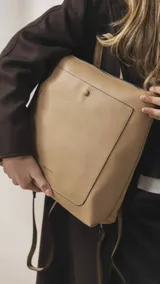 Mochila de diseño moderno y funcional, confeccionada en símil cuero con textura granulada. Cuenta con un bolsillo frontal con broche, cierre principal superior, manija superior y correas ajustables. Incluye logo de la marca grabado en el frente.