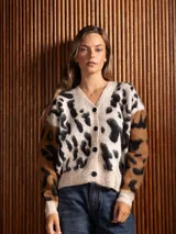 Saco tipo cárdigan de tejido suave y peludo, con estampado animal print en tonos beige, negro y marrón. Presenta cuello en V, cierre frontal con botones y mangas en contraste de color con diseño animal print.