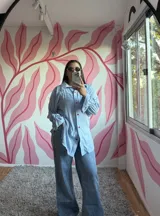 Camisa oversize de fibrana a rayas celestes y blancas, con cuello clásico, mangas largas con puños y botones frontales de acrílico en forma de corazón rojo.