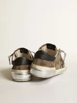 Zapatillas deportivas Golden Goose modelo Super-Star, color marrón verdoso desgastado, con estrella lateral negra y detalles en cuero negro en el talón. Presentan un acabado intencionalmente envejecido en la suela y cordones grises. En el lateral se lee el texto 'GGDB/SSTAR'.