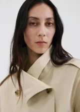 Chaqueta crop estilo gabardina corta color beige, de diseño recto, cuello alto tipo embudo, manga larga, bolsillos laterales y cierre cruzado de doble botonadura con botones oscuros. Con forro interior de poliéster.