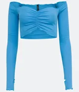 Blusa cropped de media malla color celeste, con escote hombro a hombro, mangas largas con abertura para los dedos y volantes en el escote, puños y bajo.