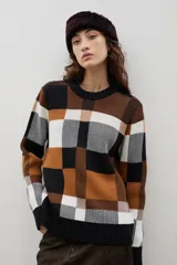 Sweater de cuello redondo con diseño jacquard a cuadros en tonos negro, blanco y marrón. Presenta un corte holgado, mangas largas y terminaciones en tejido acanalado.