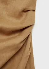 Vestido midi de lino color tostado, con diseño asimétrico de un solo hombro, manga corta y cintura drapeada con abertura lateral en el bajo.