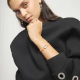 Pulsera elástica de hilo naranja con un dije central de corazón plateado y un cierre esférico plateado.