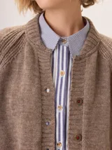 Saco de lana color marrón, de tejido grueso, con cuello redondo y botones frontales. Presenta mangas raglán con detalle de punto acanalado y bolsillos delanteros tipo parche.