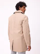 Gabardina de corte clásico en color beige, con cierre frontal de cremallera y botones, cuello camisero y puños ajustables con trabillas.