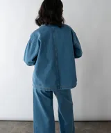 Camisa de denim azul con cuello polo, cierre frontal parcial y dos bolsillos cuadrados en el frente. Presenta un corte holgado y mangas largas.