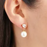 Aros colgantes dorados con dije superior de cristal blanco en forma de triángulo y dije inferior de perla redonda. Cierre de tuerca a presión.