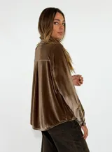 Camisa de terciopelo color bordó, con cuello mao y cierre frontal de botones. Presenta detalles de volados verticales a ambos lados de la botonera y mangas largas con puños abotonados.