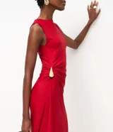 Vestido midi sin mangas color rojo, confeccionado en microfibra con elastano. Presenta un diseño drapeado en el lateral de la cintura con un adorno metálico en forma de gota, escote redondo y una abertura lateral en la falda.