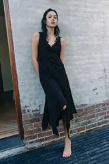 Vestido midi de viscosa color negro, sin mangas, con escote en pico adornado con encaje a tono. Presenta un detalle de nudo drapeado en la cintura y bajo asimétrico.