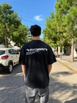 Remera negra de corte oversize con estampa gráfica blanca en la espalda que incluye el logo y texto descriptivo.