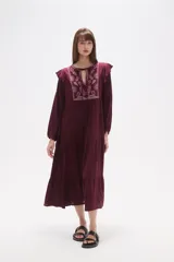 Vestido midi holgado de viscosa color vino tinto, con mangas largas y volados en los hombros. Presenta un canesú con bordado floral en tonos rosados y cuello con abertura en forma de lágrima y lazo para atar.