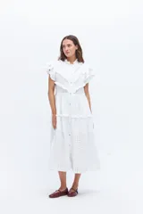 Vestido midi de lino blanco con diseño de broderie, cuello alto, cierre frontal con botones y volados decorativos en los hombros y el cuerpo.