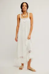 Vestido largo slip blanco de tela liviana y semitransparente, con silueta trapecio, escote cuadrado, tiras regulables, detalles de encaje, volado en el ruedo y espalda descubierta con lazo de ajuste.