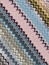 Chal o bufanda de tejido de punto con patrón de zigzag vertical en franjas multicolores, predominando tonos tierra, amarillo, gris y negro. Presenta flecos en los bordes.