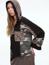 Buzo con capucha de diseño patchwork que combina paneles de tejido waffle negro, estampado camuflado y estampado floral. Presenta cierre frontal parcial con botones, bolsillo tipo parche en el pecho y mangas largas con puños.