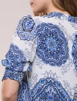 Blusa de crepe color blanco con estampado paisley en tonos azules y negros. Presenta cuello mao con escote en V, cierre frontal con botones y mangas cortas abullonadas con puños elastizados en punto smock.