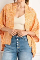 Kimono oversize color naranja con estampado floral blanco, mangas 3/4 y confeccionado en rayón.