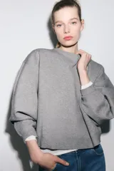 Sudadera gris de cuello redondo y manga larga, con puños y dobladillo acanalados.