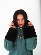 Campera de gamuza color beige con interior y detalles de corderito sintético en cuello y puños. Presenta cierre frontal con botones tipo toggle de madera y cuero, y bolsillos frontales.