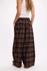 Pantalon de corte oversize y tiro medio, confeccionado en tela con estampado de cuadros en tonos marrones y negros. Presenta una silueta amplia y holgada con cintura elástica y cordón ajustable.